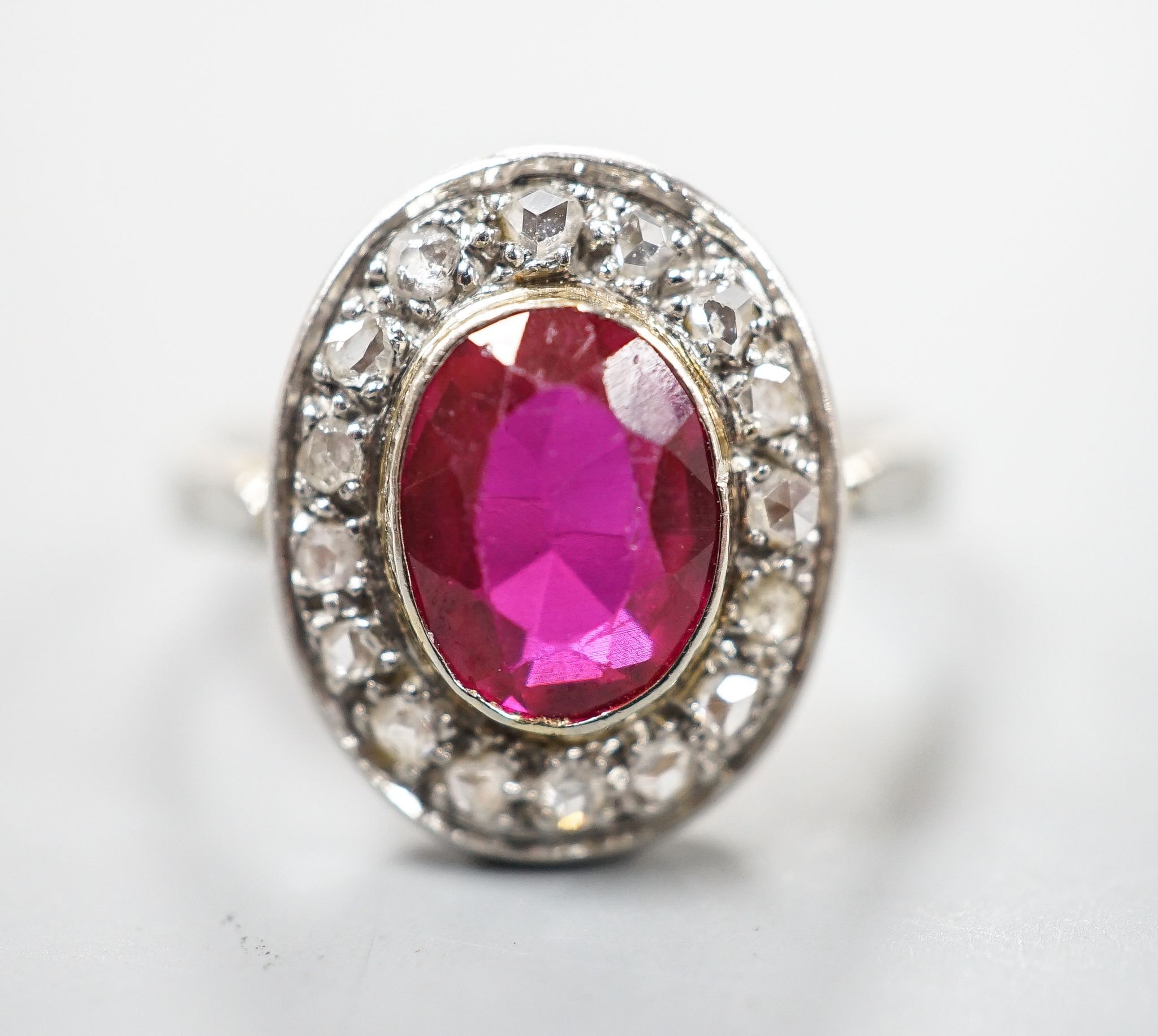 A white metal, synthetic ruby and diamond set oval cluster ring, size N, gross weight 3.4 rams.